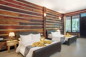 A hotel room with two beds, wooden paneling on the walls, a window with a view, and a nightstand with a lamp.