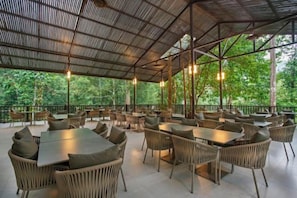 An outdoor dining area with tables and chairs, surrounded by a metal roof structure. - Rompin Rainforest Lodge (Rompin)
