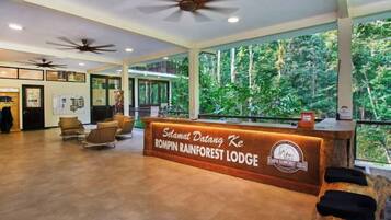 A reception area with a wooden reception desk, seating, ceiling fans, and large windows overlooking a forest.