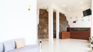 A reception area with a stone wall, a reception desk, a flat-screen TV, and a sofa. - The Dorwin Heights (Kandy)