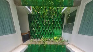 Ein modernes Atrium mit einer zentralen, begrünten Wasserspielen, weißen Wänden und verschiedenen Topfpflanzen.