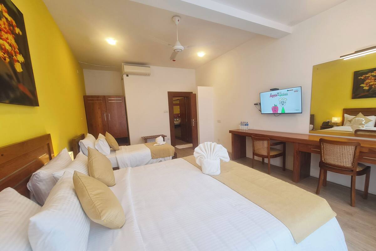 Une chambre d’hôtel avec deux lits, un bureau, une télévision et une salle de bain visible à travers une porte ouverte.