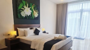 Ein Hotelzimmer mit einem großen Bett, einem Nachttisch mit Lampe, einem Blumengemälde an der Wand und Blick ins Freie durch transparente Vorhänge.