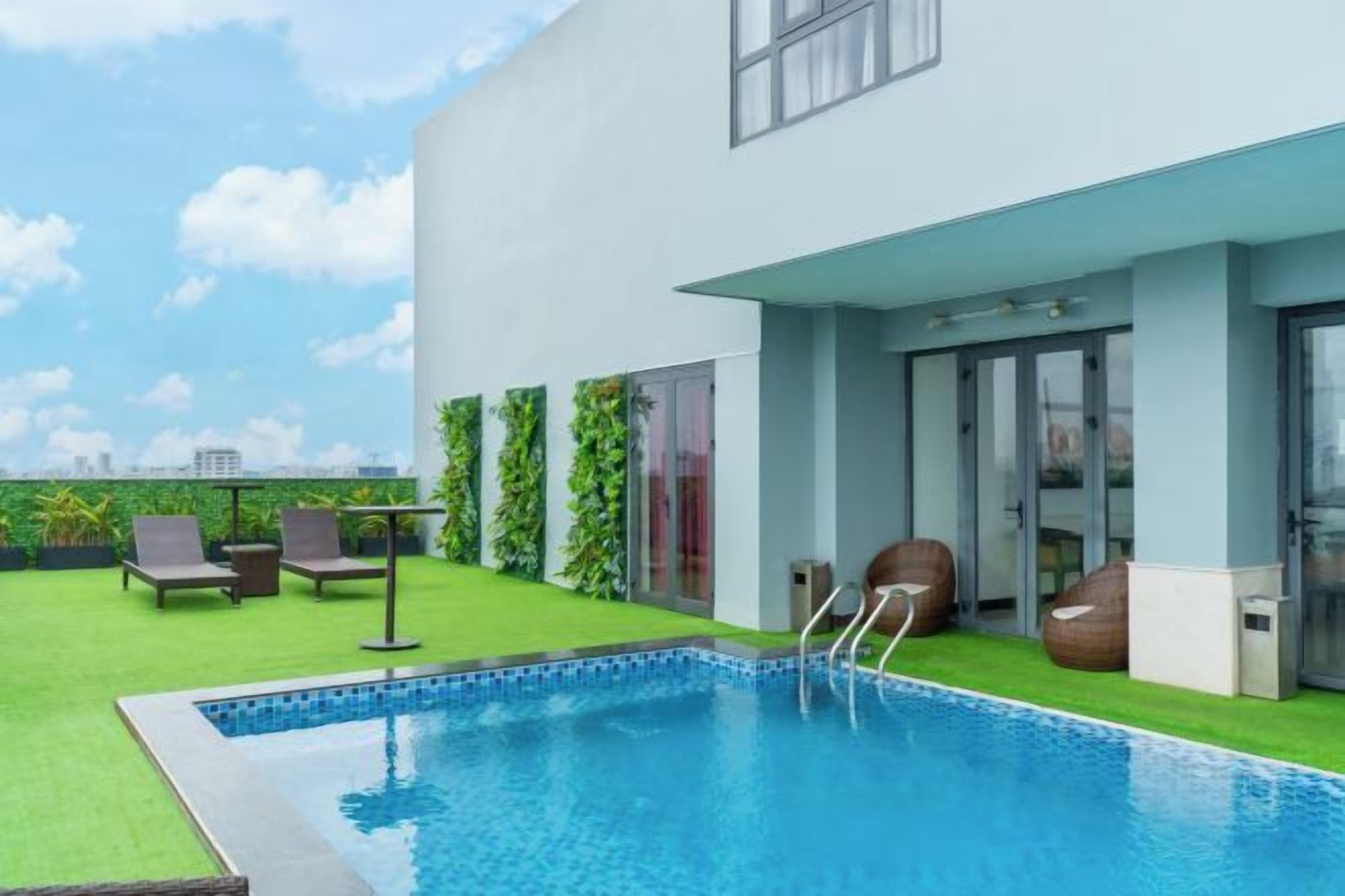 A rooftop swimming pool with a clear view of the city skyline, surrounded by a modern building with glass doors and a green lawn.