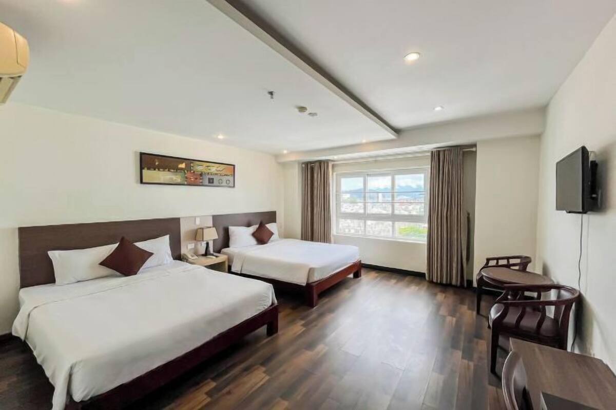 Habitación de hotel con dos camas, un escritorio, una silla, un televisor y una ventana con cortinas.