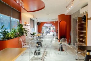 Ein modernes Interieur mit transparenten Kunststoffstühlen, einer langen Theke und Blick auf die Straße durch große Fenster.