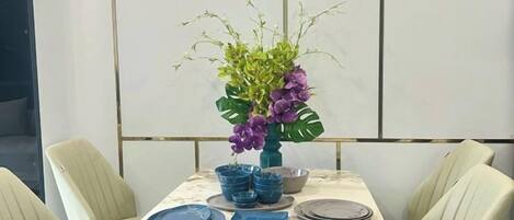 Una mesa de comedor dispuesta con platos azules y un jarrón con flores moradas.