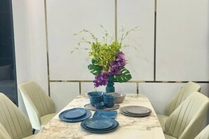 A dining table set with blue plates and bowls, a vase with purple flowers, and a marble table surface. - Homestay SWAN BY KAT (Nghia Tru)