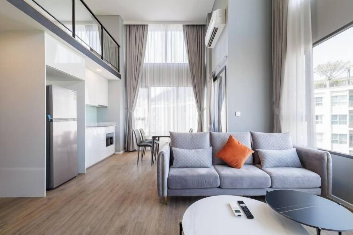 Ein modernes Wohnzimmer mit einem grauen Sofa, einem runden Couchtisch und einem Essbereich mit Stühlen.