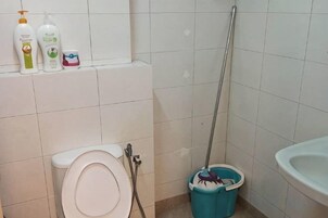 Un baño con inodoro, lavamanos y cubo de limpieza.