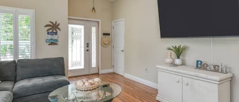 A living room with a sofa, a glass coffee table with a basket, a flat-screen TV mounted on the wall, and a cabinet with decorative items.