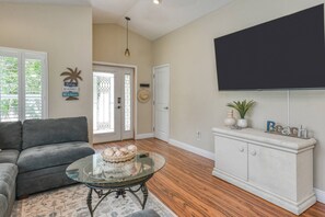 A living room with a sofa, a glass coffee table with a basket, a flat-screen TV mounted on the wall, and a cabinet with decorative items.