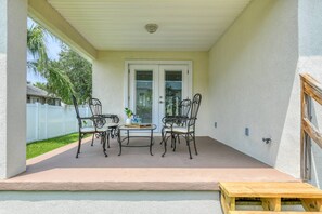 A covered patio area with a table and chairs, a small table with a vase, and a wooden bench.