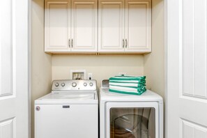 A laundry area with a Maytag washer and dryer, a countertop with a coffee maker, and a stack of green and white towels.