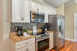 A kitchen with white cabinets, a stainless steel refrigerator, a microwave, a coffee maker, and a granite countertop.