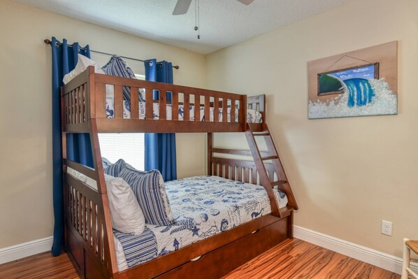 Una cama litera con escalera, una ventana con cortinas azules y un cuadro de una ola en la pared.