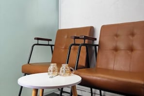 Una habitación con dos sillones de cuero marrón, una mesita redonda pequeña con dos jarras de vidrio transparente y una pared blanca.