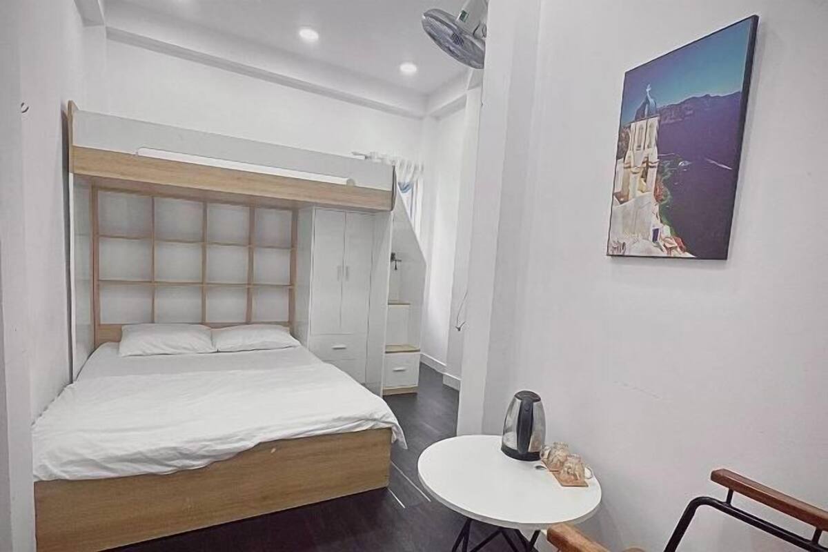 Un dormitorio con una cama, una mesita redonda con una tetera, una silla y un cuadro en la pared.