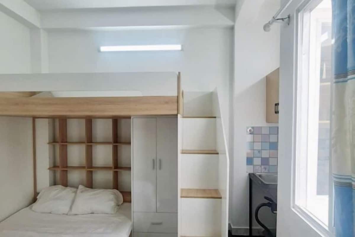 Un dormitorio con cama, armario, estantería y ventana con cortinas.