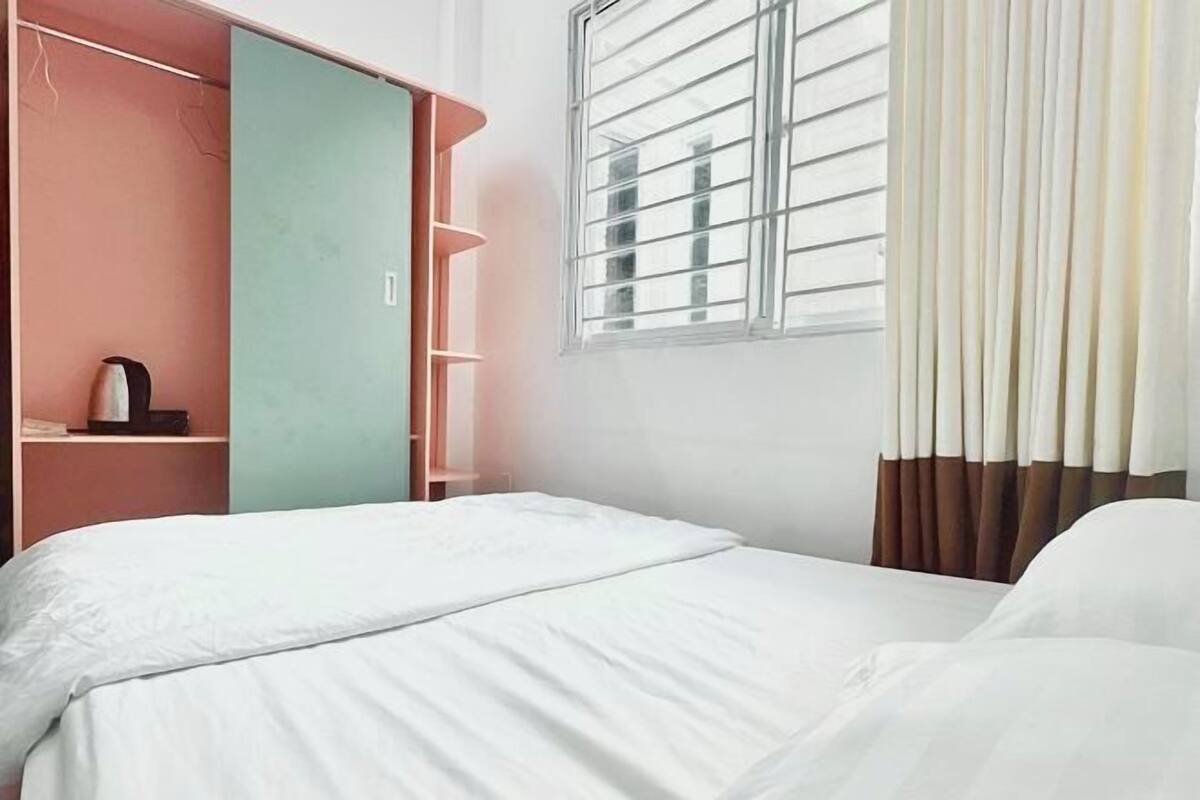 Un dormitorio con cama, armario, ventana con cortinas y estante con hervidor.