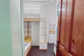 Un pasillo estrecho con una litera, estanterías blancas y un armario de madera.