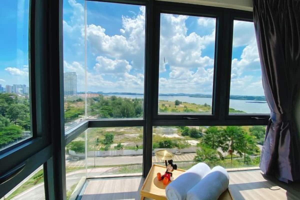 A room with a large window offering a view of a lake, greenery, and distant buildings.