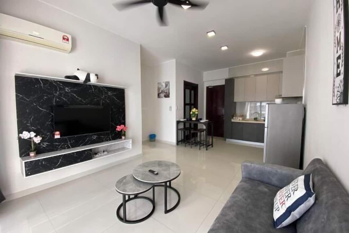 A modern living room with a flat-screen TV, a sofa, a coffee table, and a dining area with a kitchen in the background.