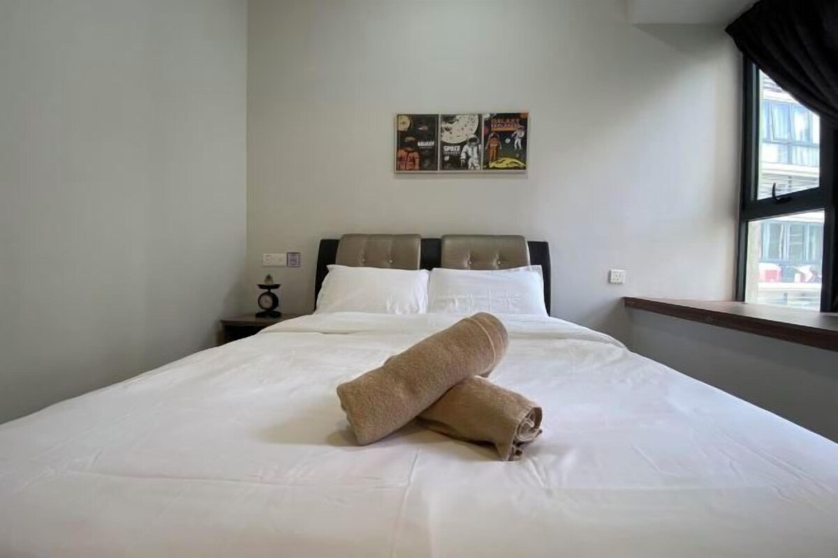 A hotel room with a bed, a nightstand, a wall clock, and a window with curtains.