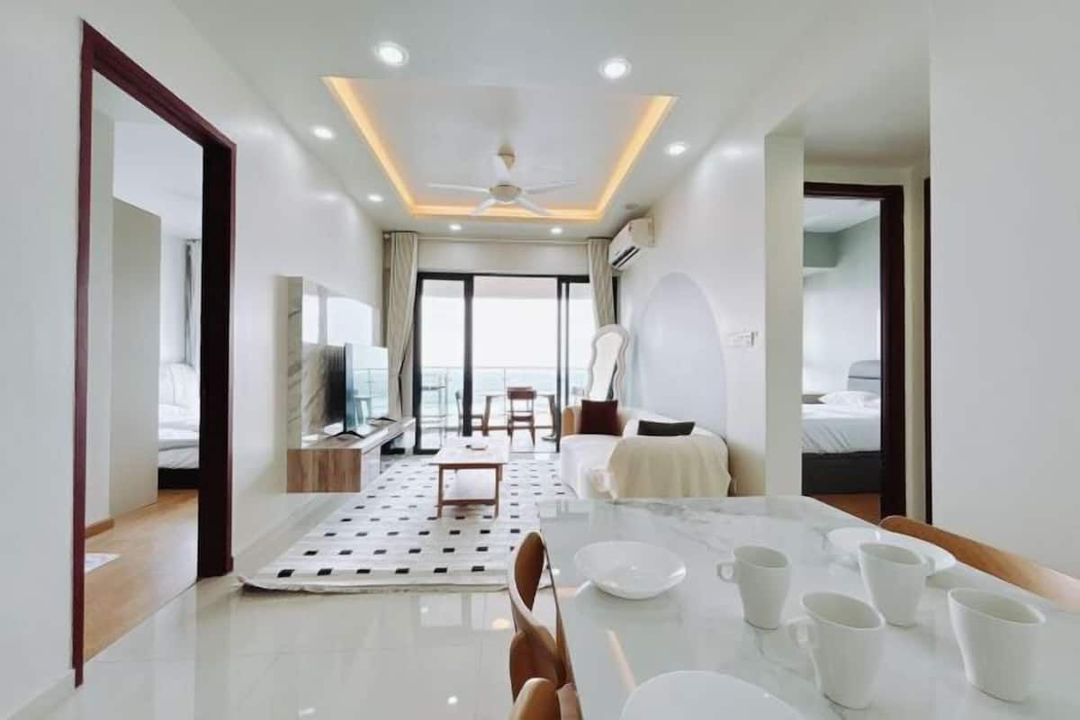 A modern hotel room with a dining area, a bed, a TV, and a view of the sea.