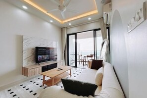 A modern living room with a sofa, a coffee table, a TV, and a balcony with a view. - Scenic Country Garden Danga Bay by Lions Bay (Johor Bahru)