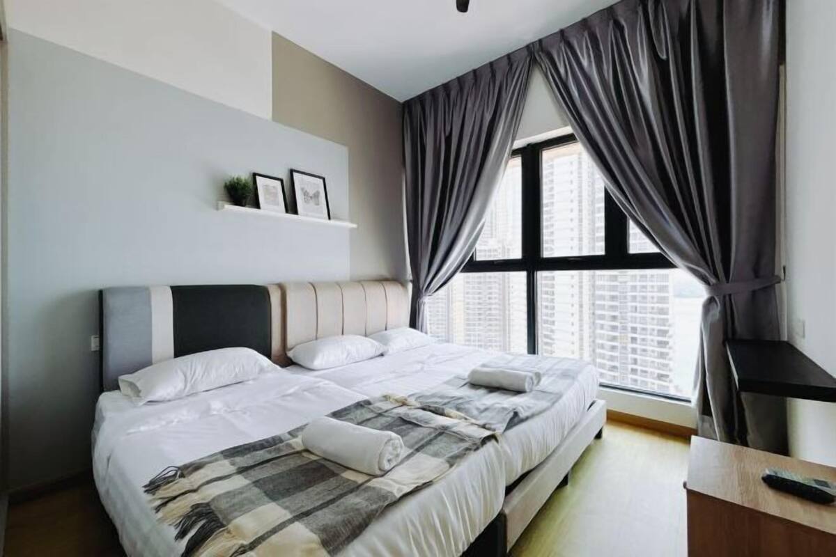 A modern hotel room with a large bed, a bedside table, a window with curtains, and a wall-mounted shelf with pictures.