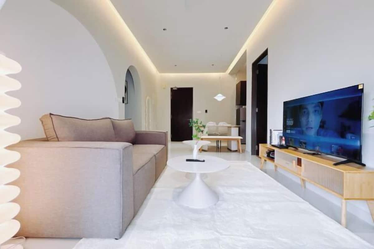 A modern living room with a sofa, a coffee table, a TV, and a hallway.