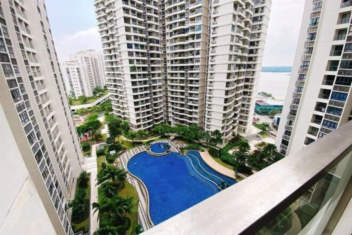 A high-rise residential building with multiple balconies, a central swimming pool, and surrounding greenery.