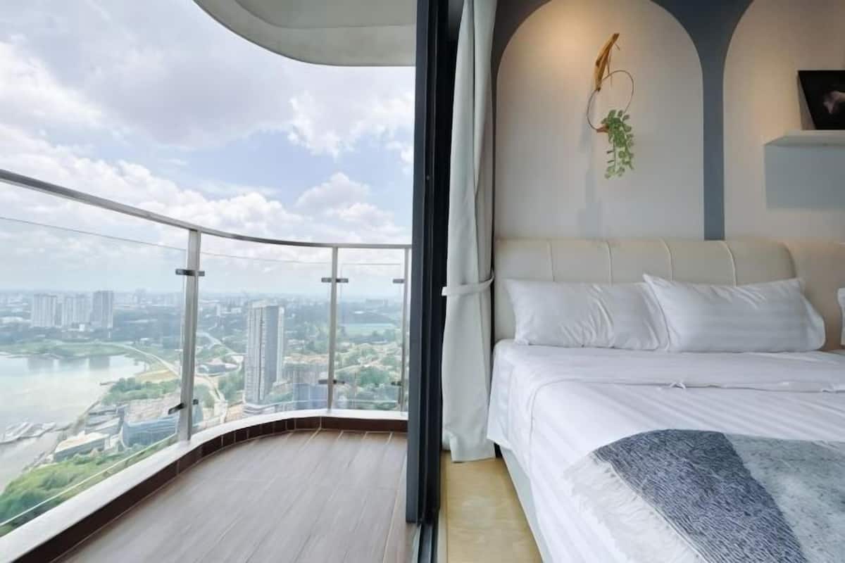 A bedroom with a bed, a view of a cityscape, and a balcony with a railing.