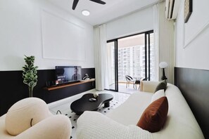 Et moderne hotelværelse med en stor seng, et opholdsområde med et sofabord, et fjernsyn og en balkon med udsigt over byen.