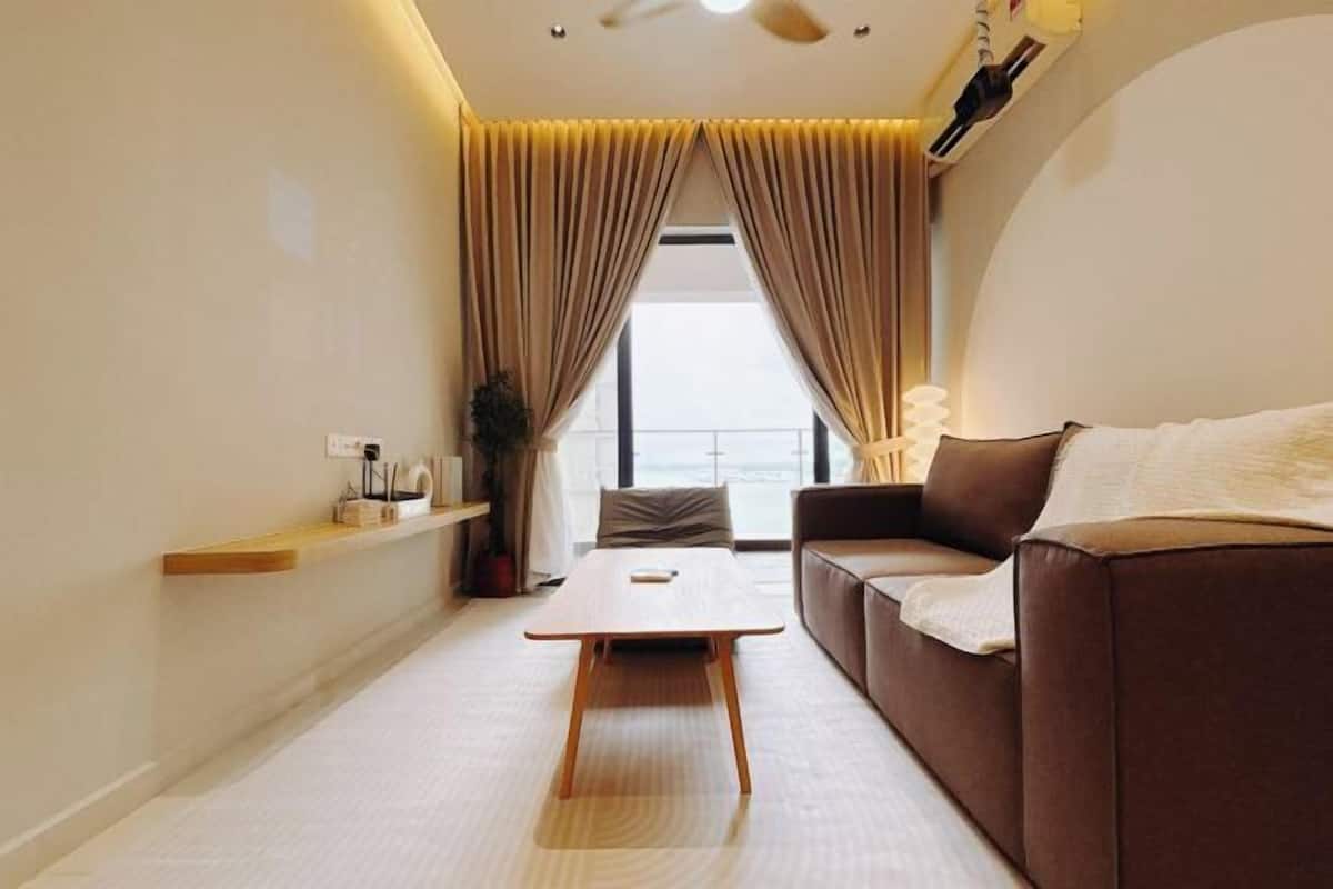 A modern living room with a sofa, a coffee table, and a view through a large window.