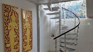 A modern interior with a spiral staircase, two large decorative panels, and a view through a window. - Rock Resort Koh Larn (Koh Larn)
