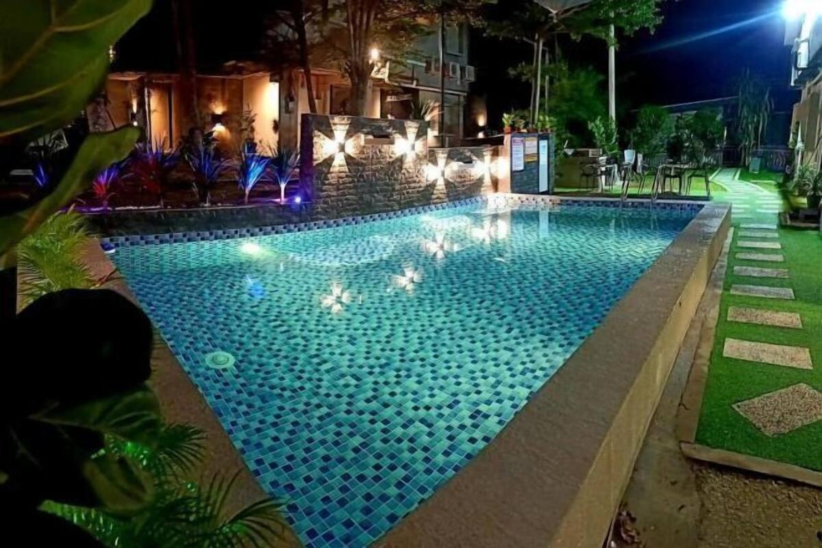 Una piscina con diseño de mosaicos, rodeada por un paseo bien iluminado y vegetación.