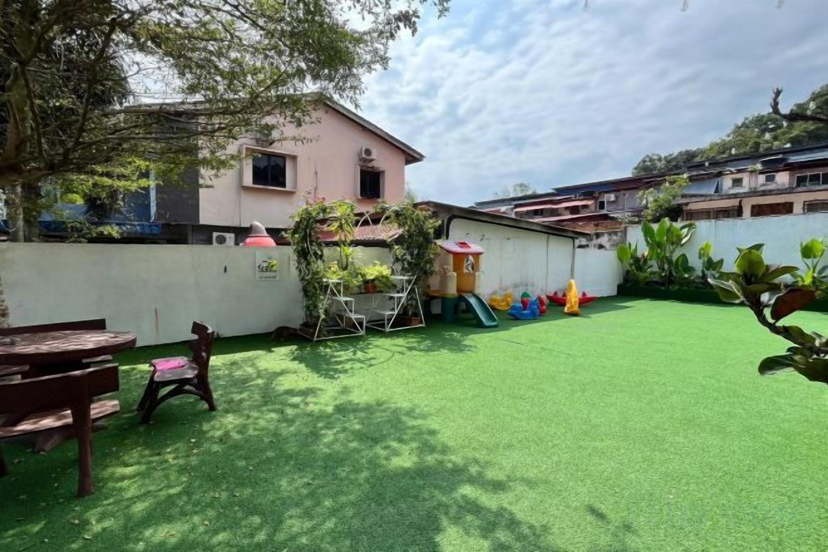 Un patio trasero residencial con césped artificial, un área de juegos y una casa rosa.