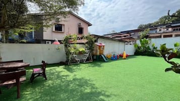 A residential backyard with artificial grass, a play area, and a pink house.