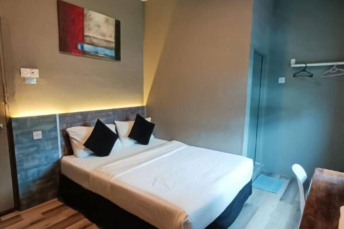 Una cama individual con cabecera, una lámpara fijada a la pared y una puerta con perchero.