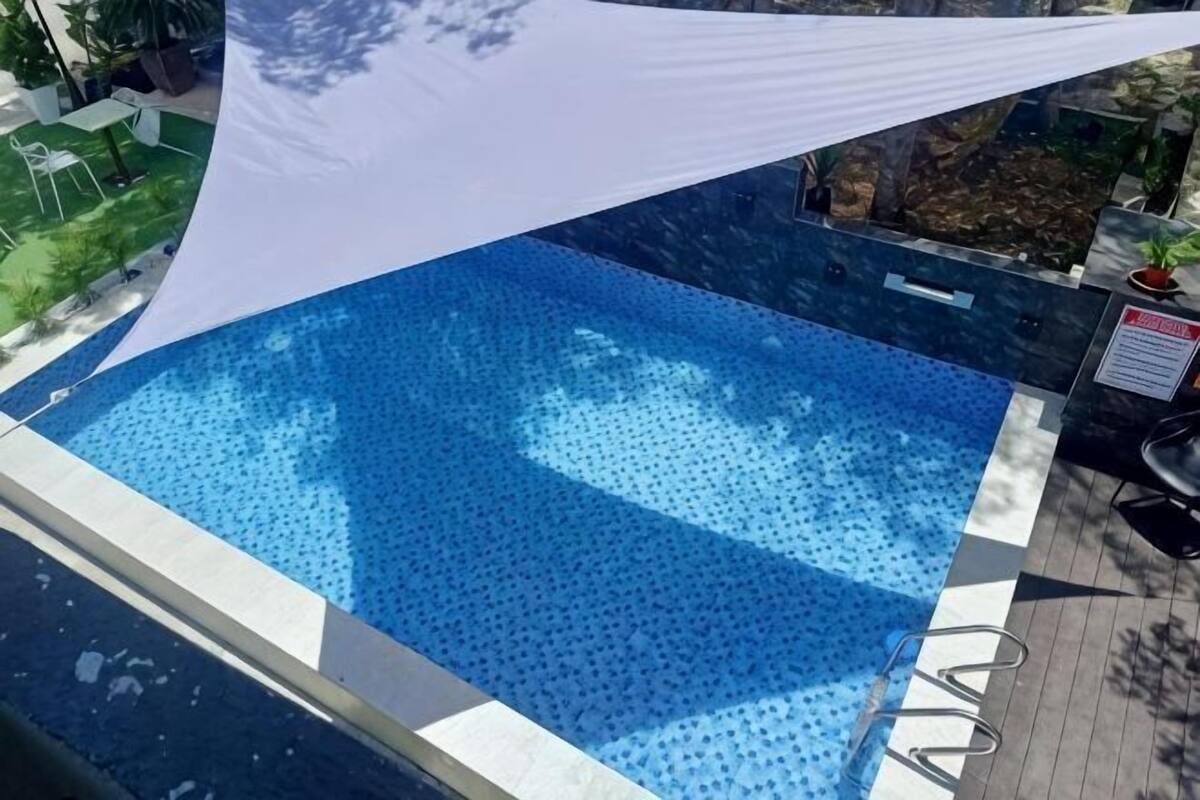 Una piscina con una vela de sombra blanca, un borde de piedra y una planta en maceta cerca.