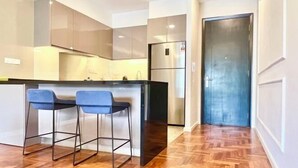 Une cuisine moderne dotée d’un îlot central, de deux tabourets de bar, d’appareils électroménagers en acier inoxydable et d’un parquet en bois disposé en motif chevrons.