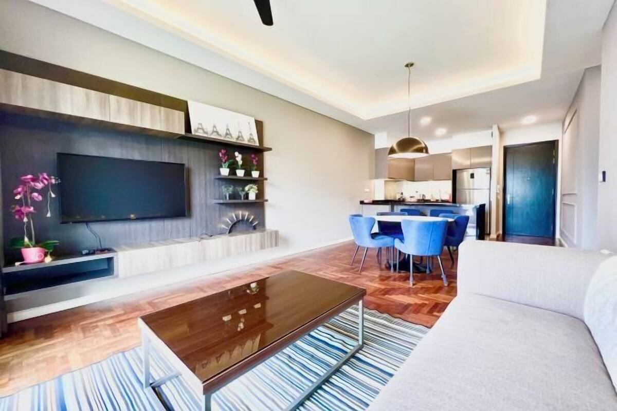 Una sala de estar moderna con una televisión de pantalla plana, una mesa de centro de madera, un sofá y un comedor con sillas azules.