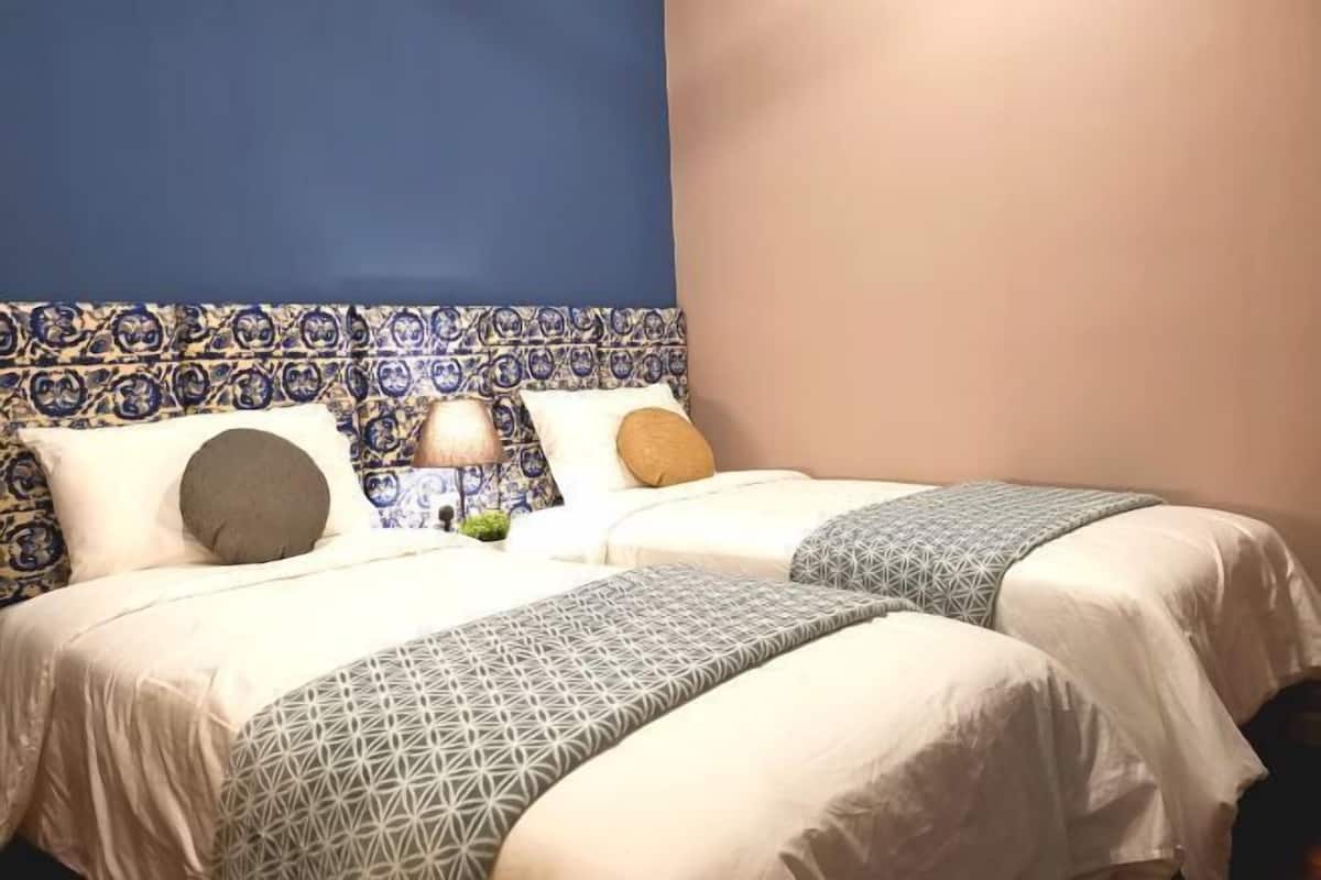 Habitación de hotel con dos camas, un cabecero estampado y una mesita de noche con lámpara.