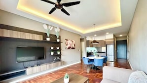 Un salon moderne doté d’un téléviseur à écran plat, de planchers en bois, d’un ventilateur de plafond et d’un coin repas avec des chaises bleues.