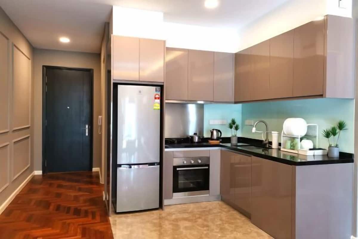 Cocina compacta con refrigerador, horno y lavamanos, que presenta gabinetes de madera clara y un piso con estampado de espiga.