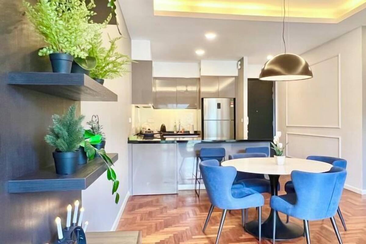 Una cocina moderna con una isla central, sillas azules alrededor de una mesa redonda y plantas en macetas sobre estantes.
