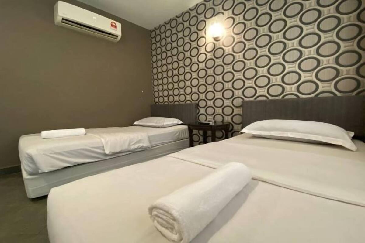 Une chambre d’hôtel avec deux lits, un climatiseur fixé au mur et un papier peint à motifs.