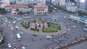Een levendig stadsplein met een centraal monument, omringd door gebouwen en voertuigen.